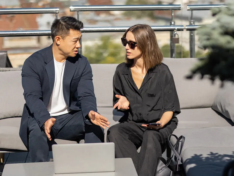 Two colleagues in conversation over a laptop on a rooftop terrace above the city