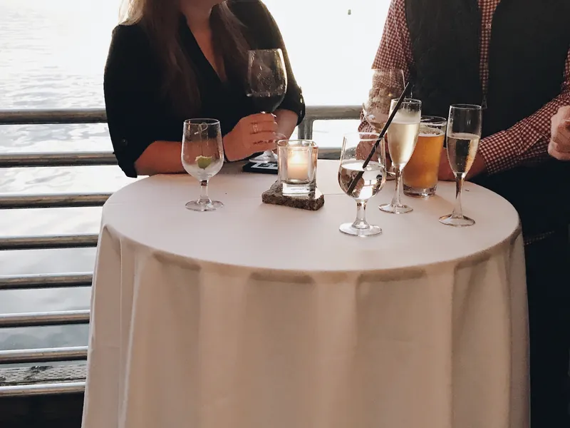 Guests talking over drinks at a candlelit standing table by the water