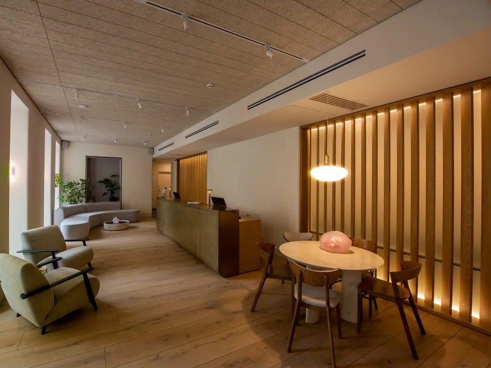 A hotel lobby with lounge chairs, a timber reception desk and warm light