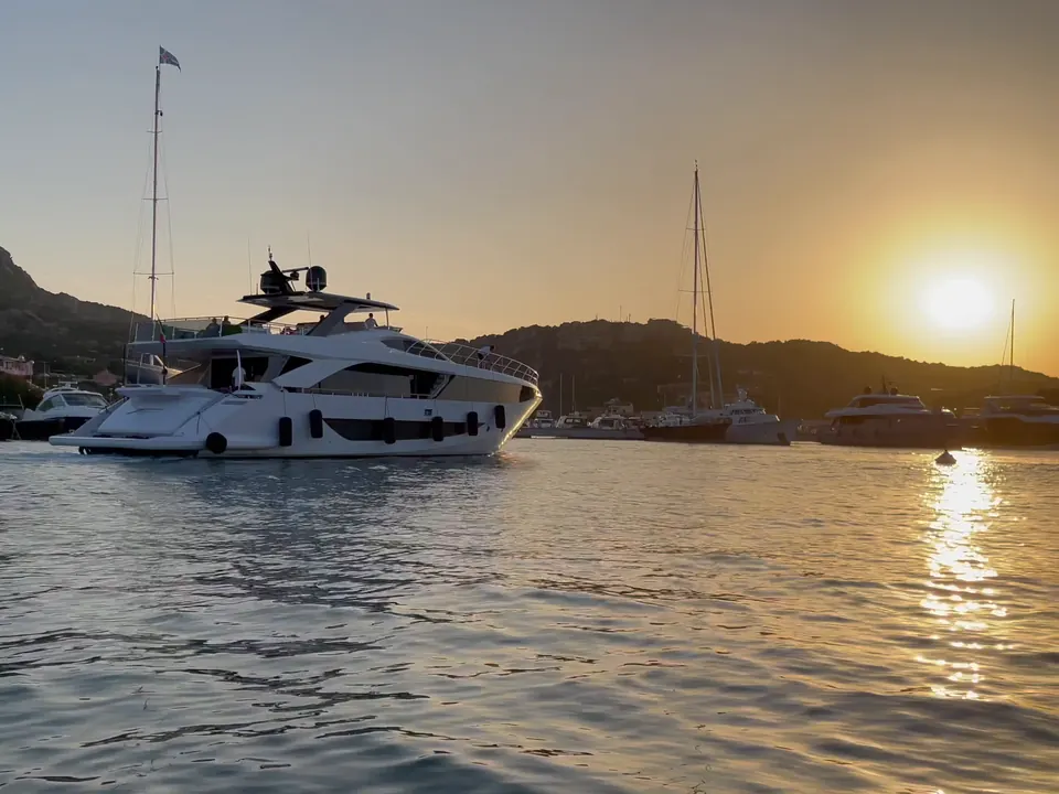 A motor yacht at anchor in a bay as the sun sets over the hills