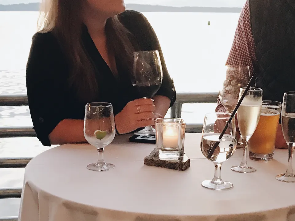 Glasses and a lit candle on a table by the water as two guests talk in the evening