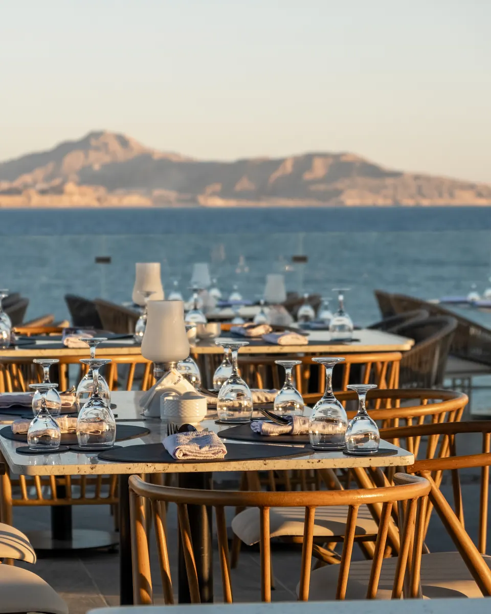Tables set with glasses on a terrace above the sea, an island on the horizon in evening light
