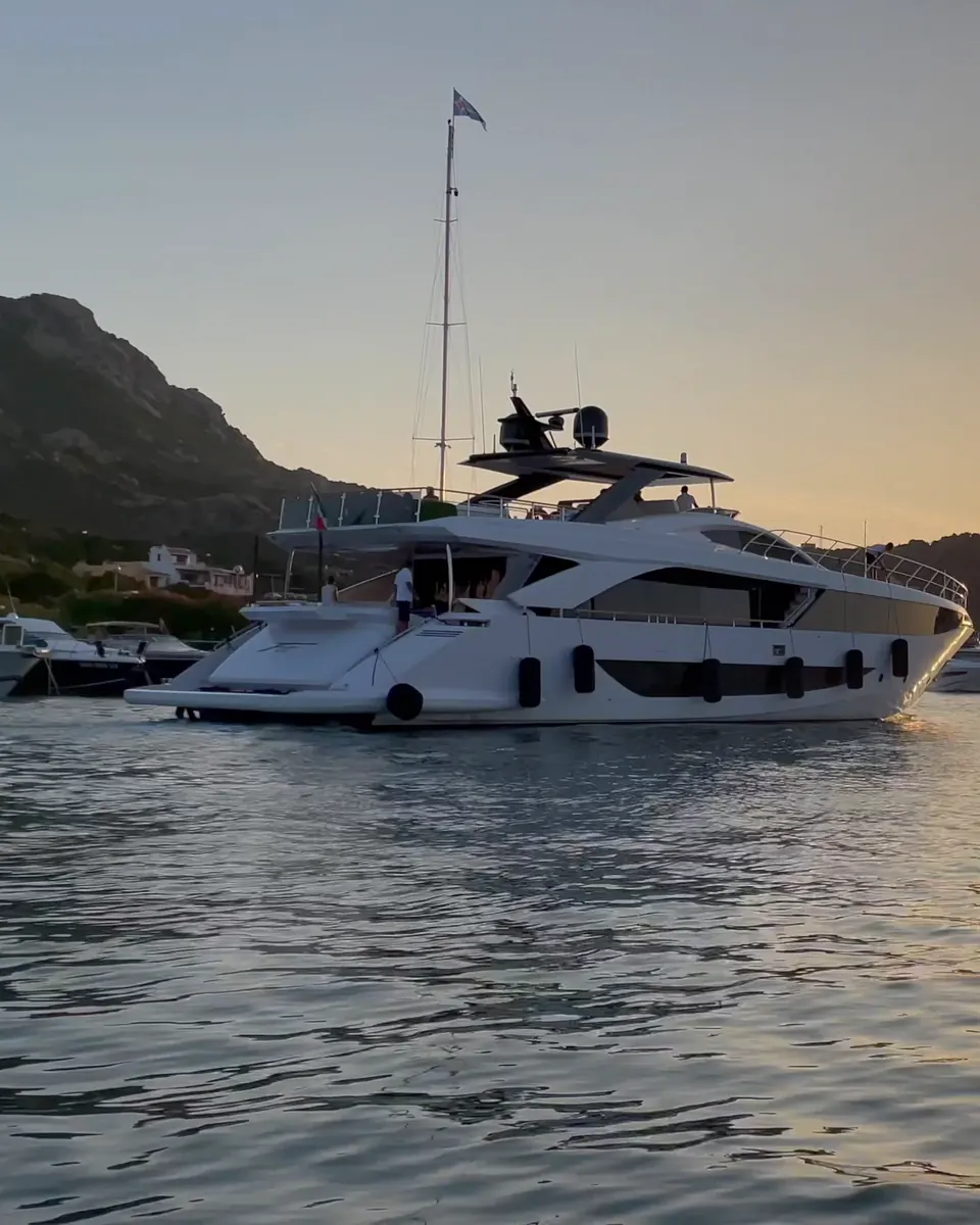 A motor yacht at anchor in a harbour as the sun sets behind the hills