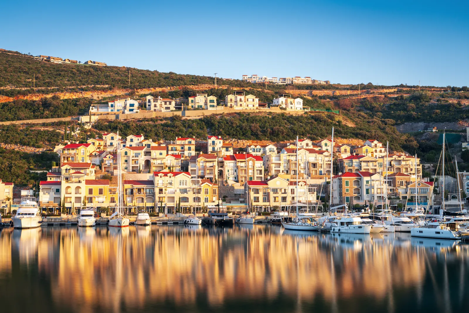 Waterfront village and marina in early golden light, yachts moored along the quay