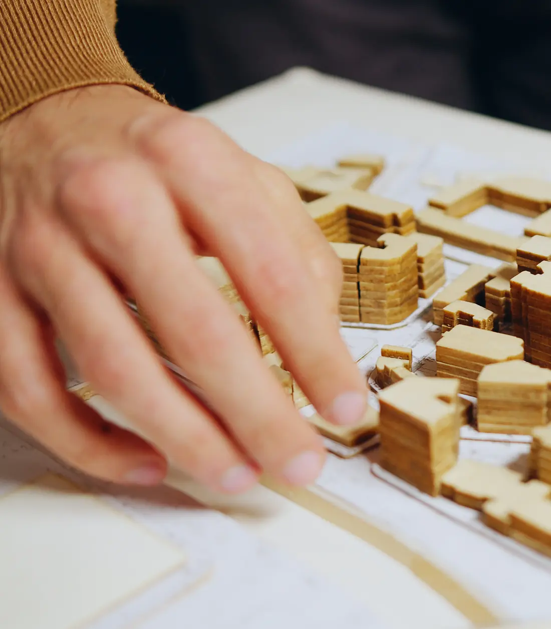 A hand setting a wooden block into an architectural model of a new district