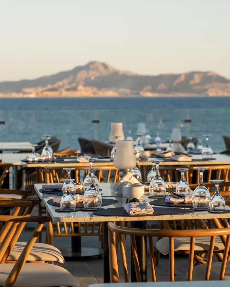 Tables set for dinner on a terrace above the sea, an island on the horizon