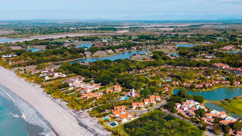 Aerial view of a beachfront community with a golf course and lagoons beside the ocean