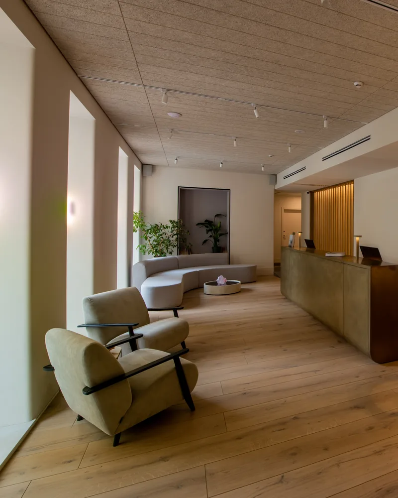 A hotel lobby with lounge chairs, a timber reception desk and warm light