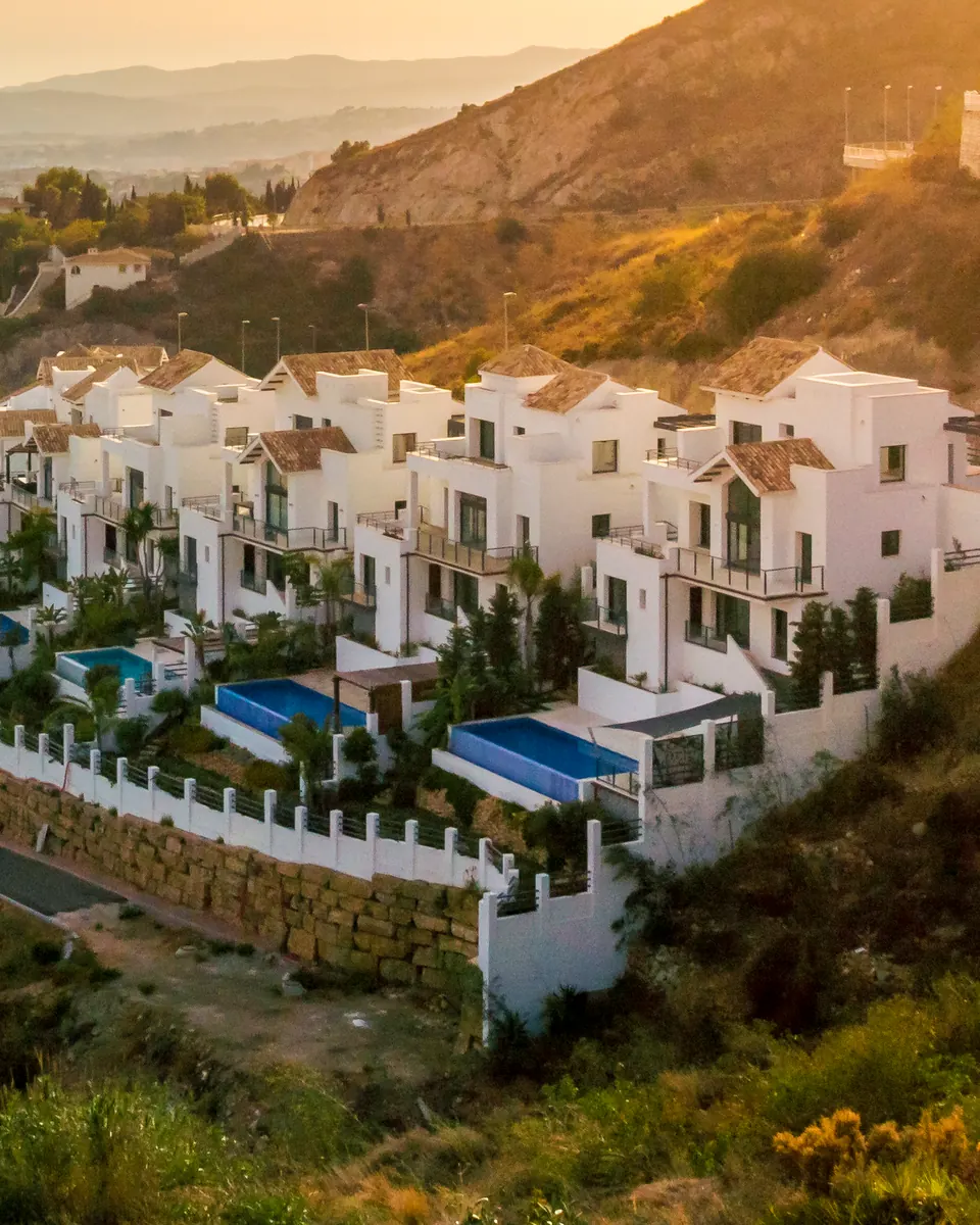 White villas with blue pools on a hillside in warm evening light