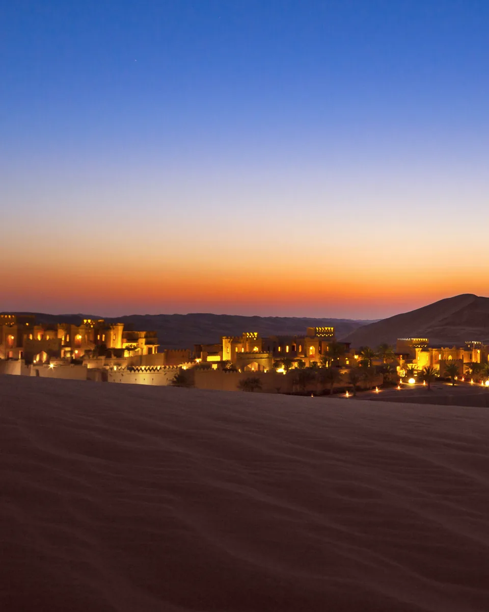 A desert resort lit at dusk among the dunes