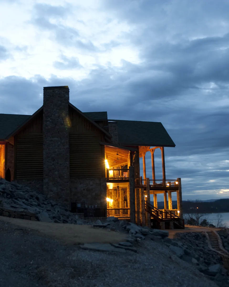 A timber lodge with lit windows on a lakeshore under an evening sky