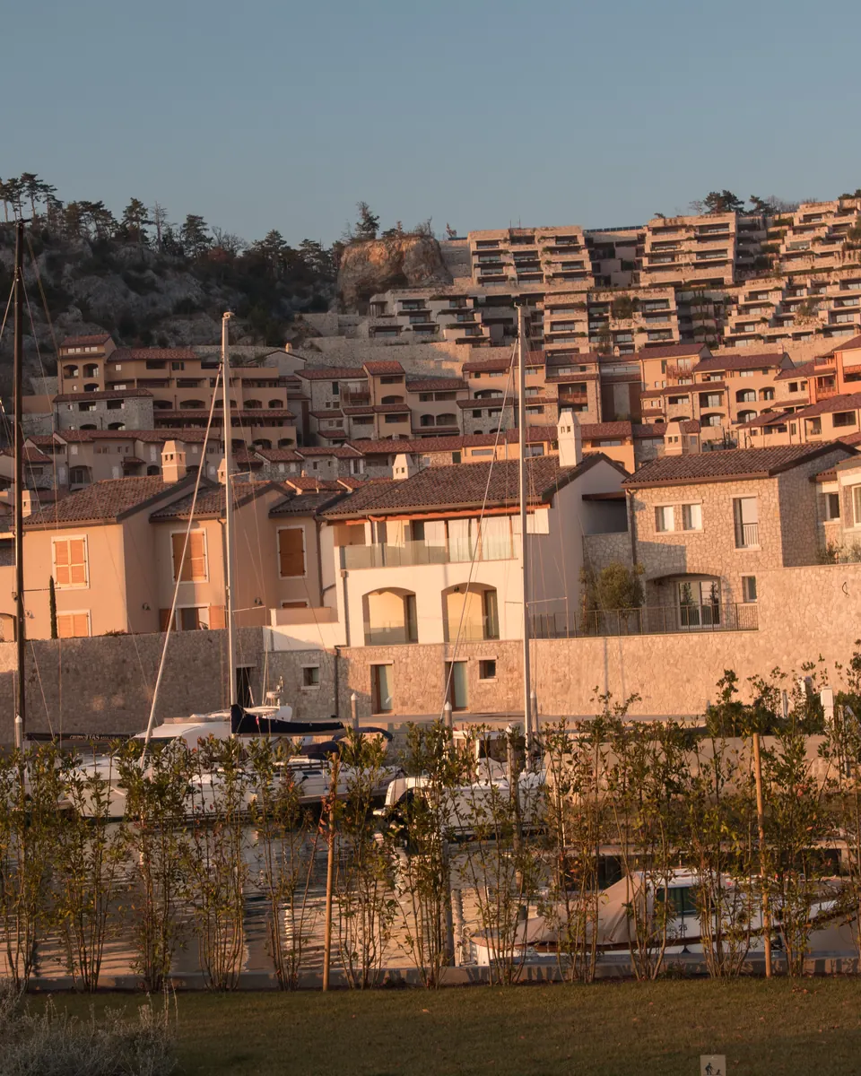Stone houses and terraced apartments above a marina in low evening sun