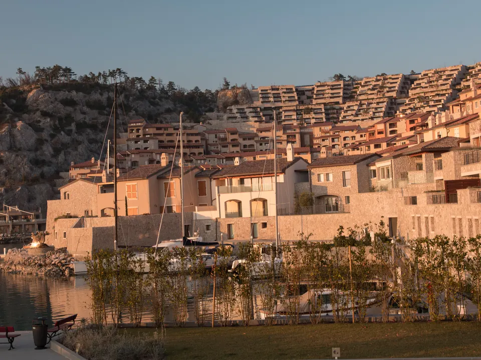 Stone townhouses stepping up a rocky hillside above a small marina at golden hour
