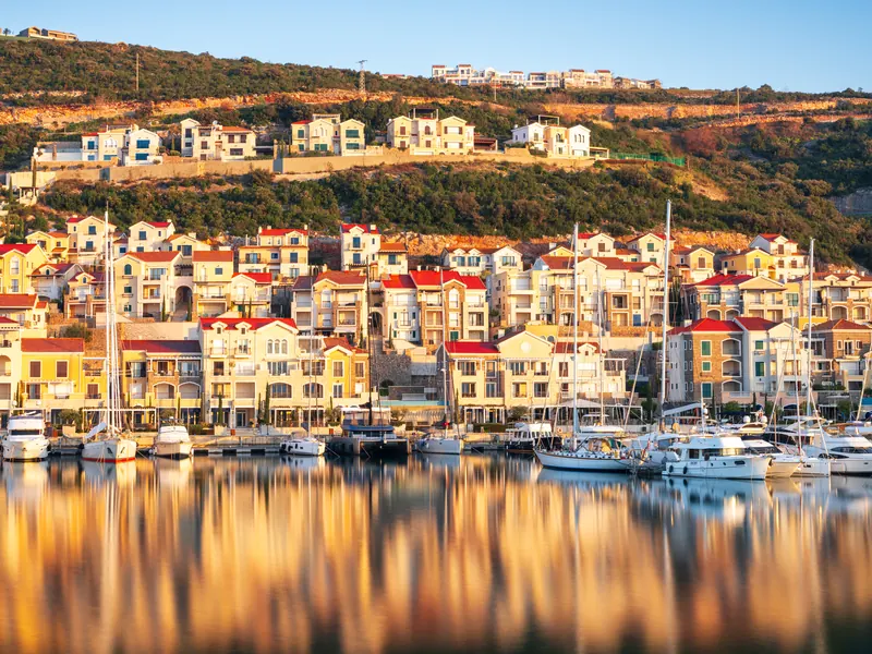 A harbour village of terraced houses above a marina at dawn, reflected in the still water