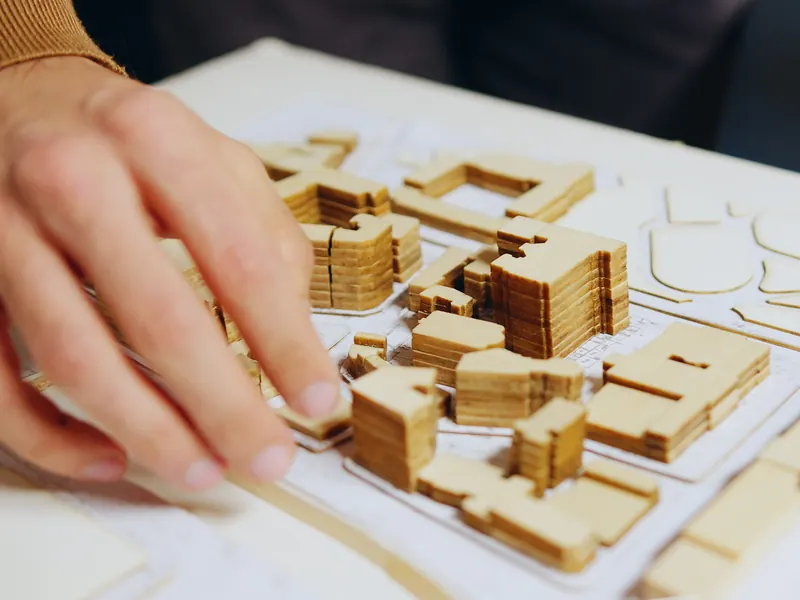 An architect’s hand adjusting a wooden city model laid out on a plan
