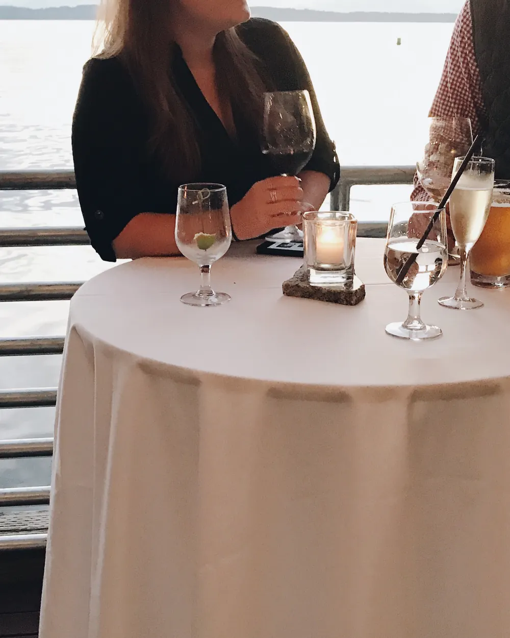 Two guests talking over drinks at a candlelit standing table above the water