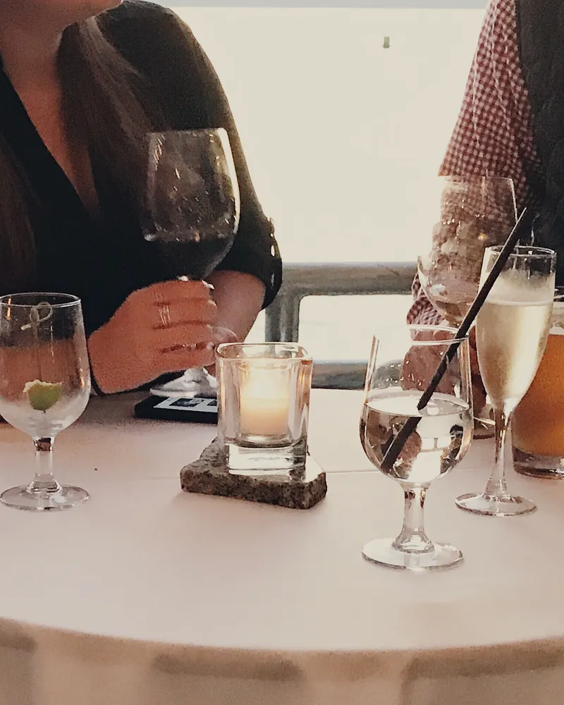 Guests talking over drinks at a candlelit standing table by the water