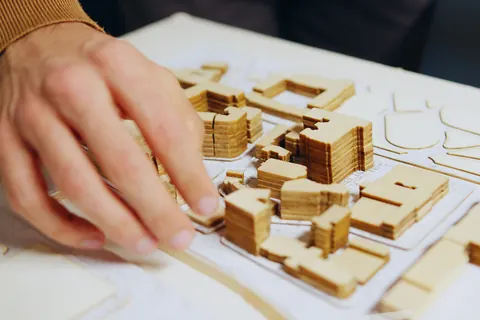 A hand setting a wooden block on an architectural site model