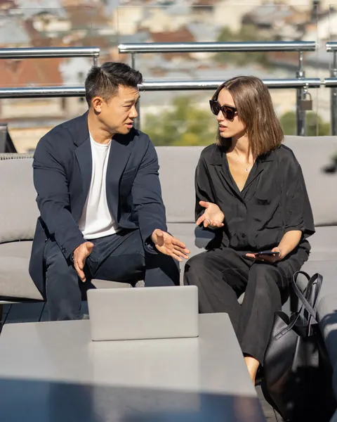 Two colleagues in conversation on a rooftop terrace above an old town