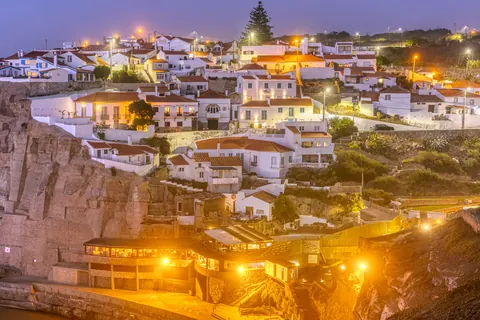 A whitewashed village lit at dusk on a cliff above the sea