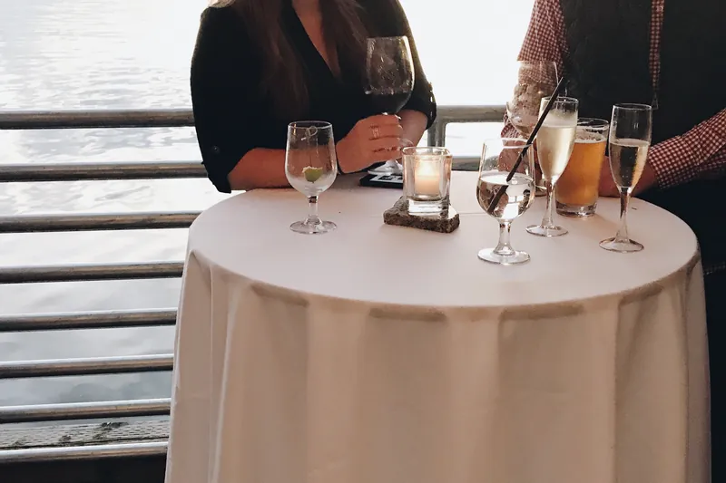 Two guests with drinks at a candlelit table on a terrace above the water