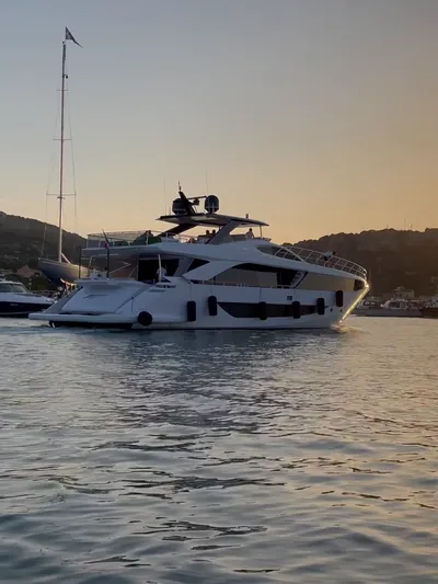 A motor yacht in a marina, the sun low over the hills behind