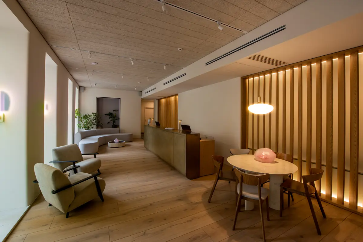 A hotel lobby with a reception desk, lounge chairs and a round table under a warm pendant light