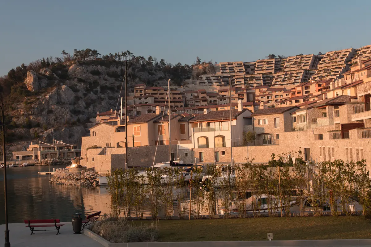 A terraced harbour village above a marina in warm evening light