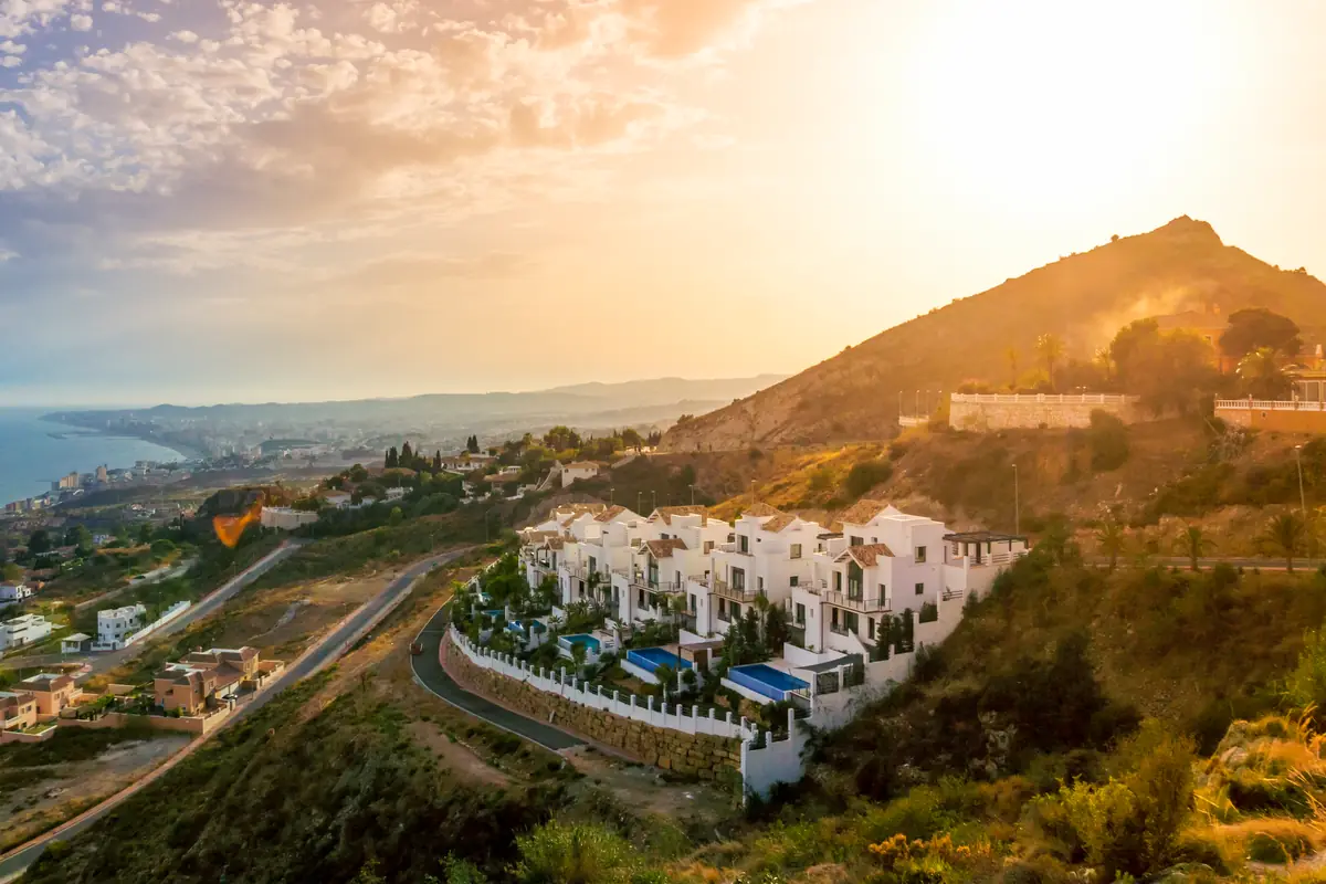 White hillside villas with private pools above the coast at sunset