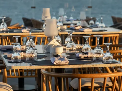 Glasses and folded napkins set on a table above the sea in the evening sun