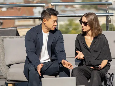 Two colleagues in conversation on a rooftop terrace above a city
