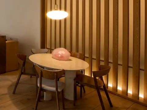 A calm lounge with a round table, oak floors and warm slatted light