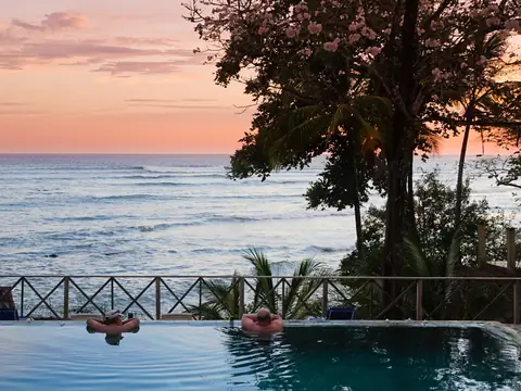 Two guests resting at the edge of an infinity pool above the sea at sunset