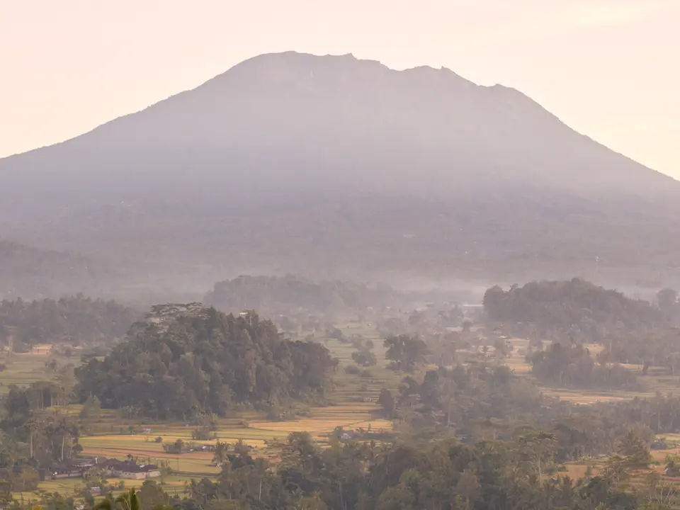 A volcano rising over a misty valley of palms and rice terraces at dawn