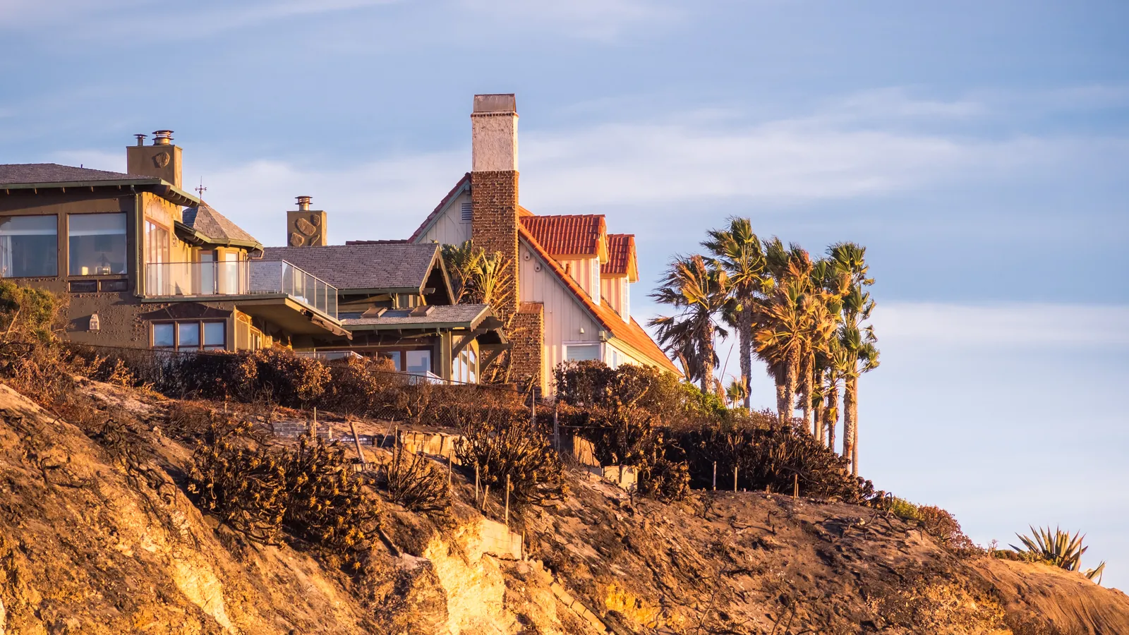 Houses with tall chimneys and a row of palms on a clifftop above the sea in the last light of the day