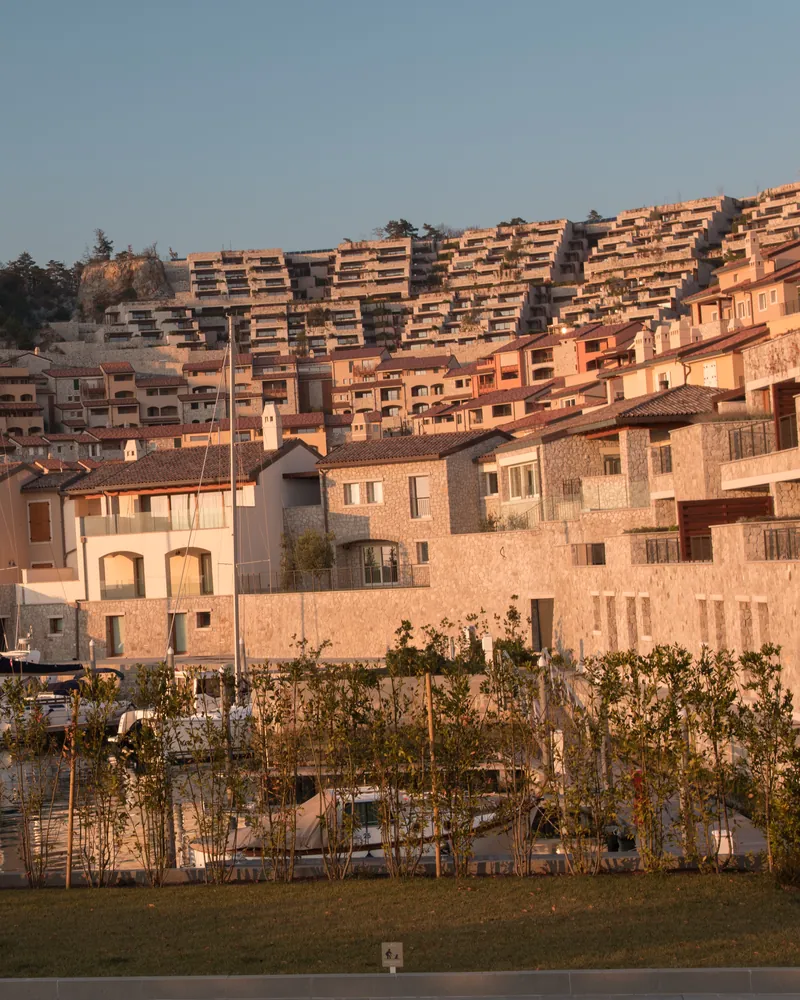 Terraced stone apartments rising above a small harbour in golden light