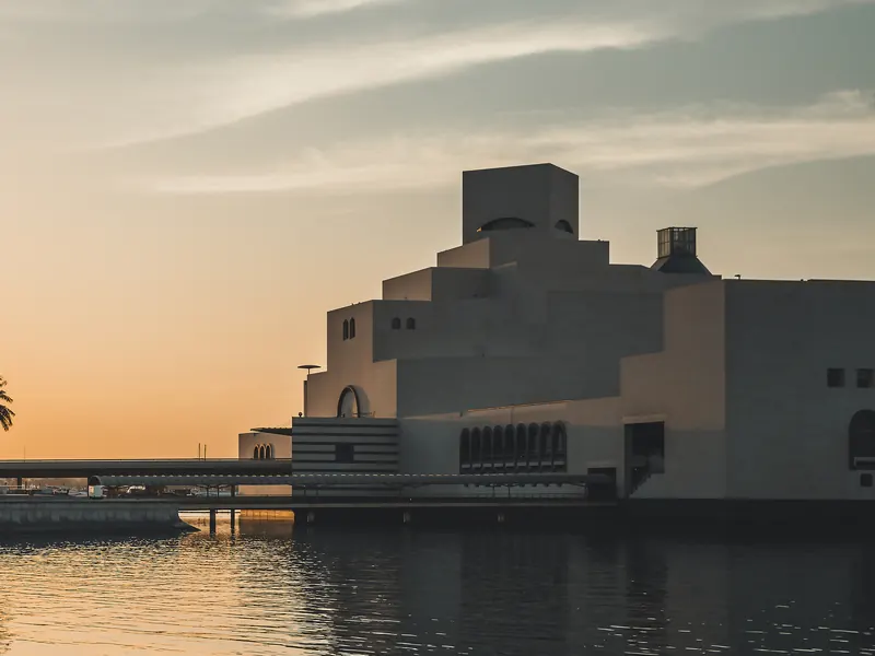 A stepped stone building on the waterfront at dusk, reflected in calm water