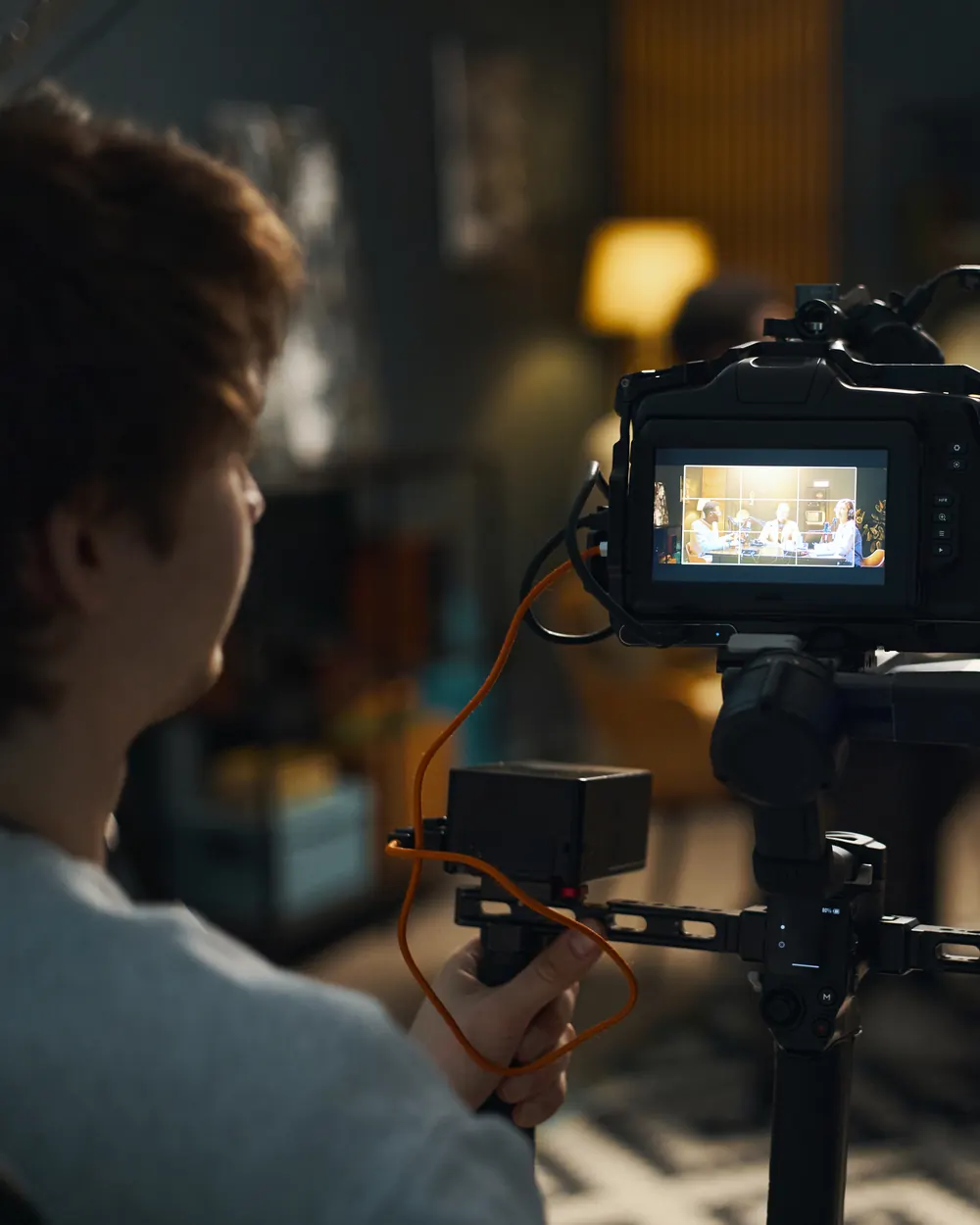 A camera operator frames an interview, the shot showing on the screen of the camera on its stabiliser