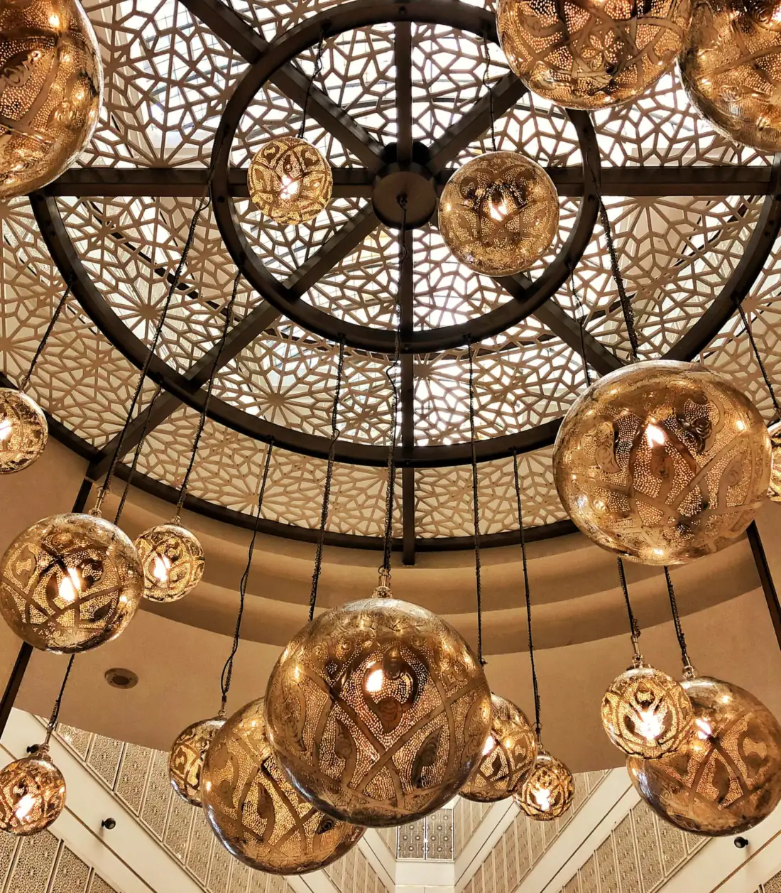 Brass pendant lamps, pierced with patterns and lit from within, hanging beneath a carved lattice dome