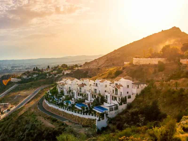White villas with pools on a hillside above a coastline at sunset