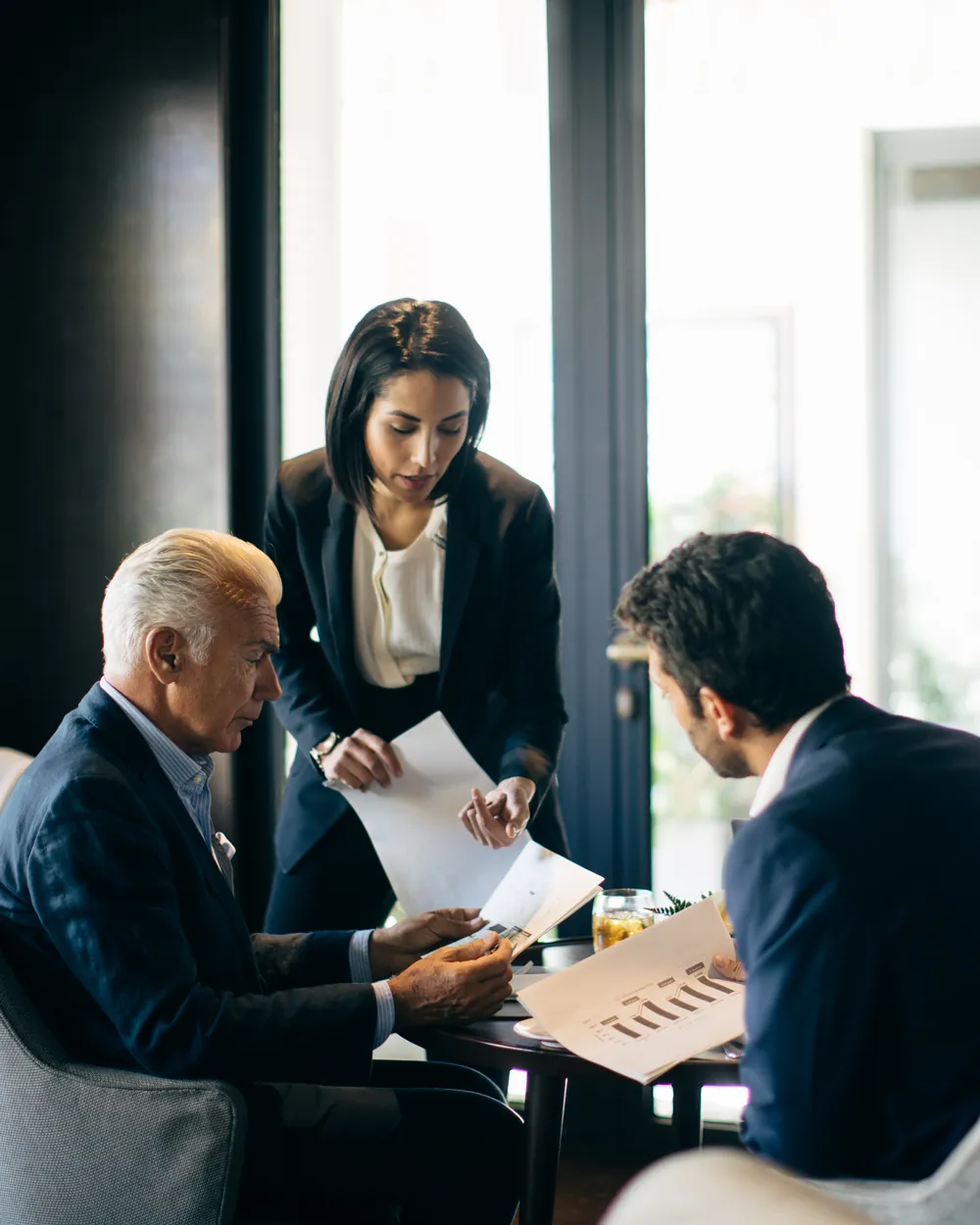Three executives reviewing papers together at a low table in a hotel lounge