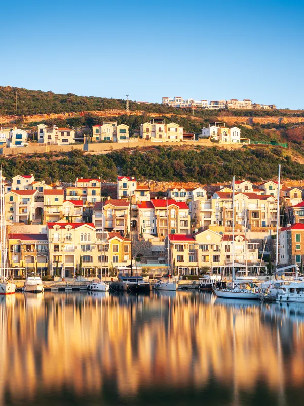 Waterfront houses above a marina, mirrored in still water at sunrise