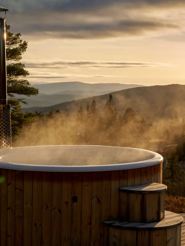 Wooden hot tub steaming above a forested valley in low sun